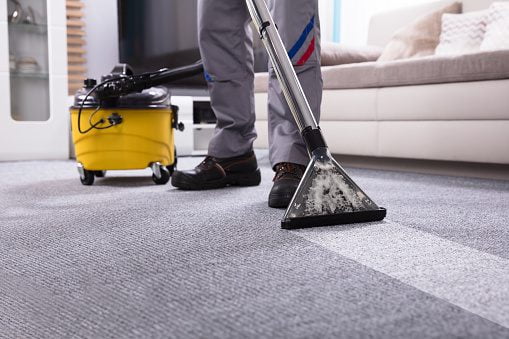 Low Section Of A Person Cleaning The Carpet With Vacuum Cleaner In Living Room